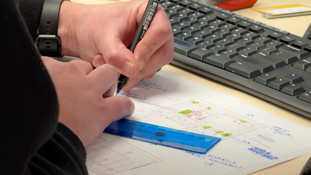 A close up of a person drawing on plans with a pen and ruler